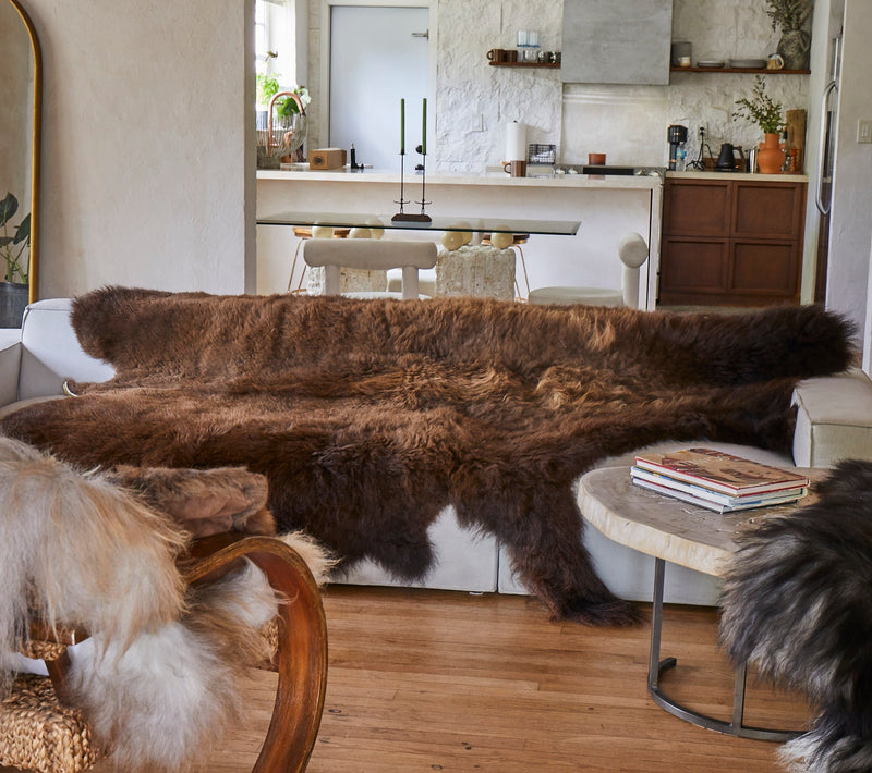 Living room with a fur throw draped over a sofa, wooden floor, and kitchen in the background.