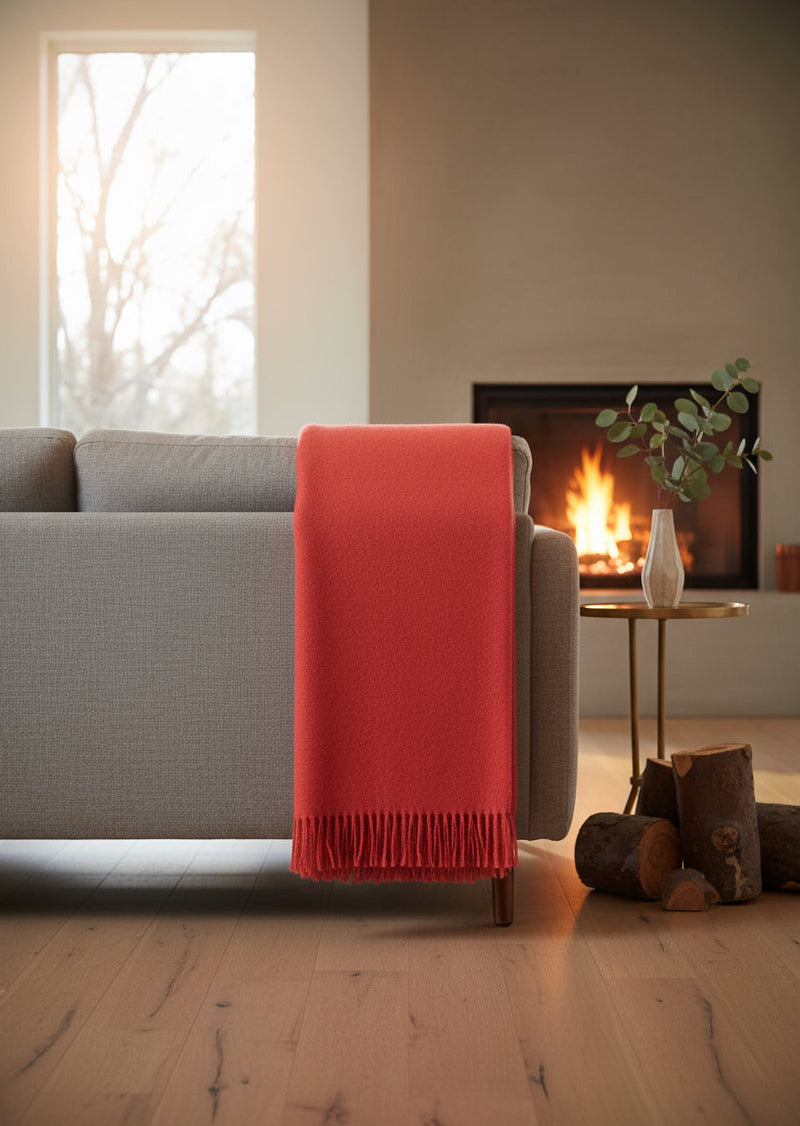 Red alpaca blanket draped over a gray sofa in a cozy living room with a fireplace.
