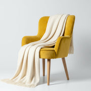Yellow chair with a white blanket draped over it on a light gray background