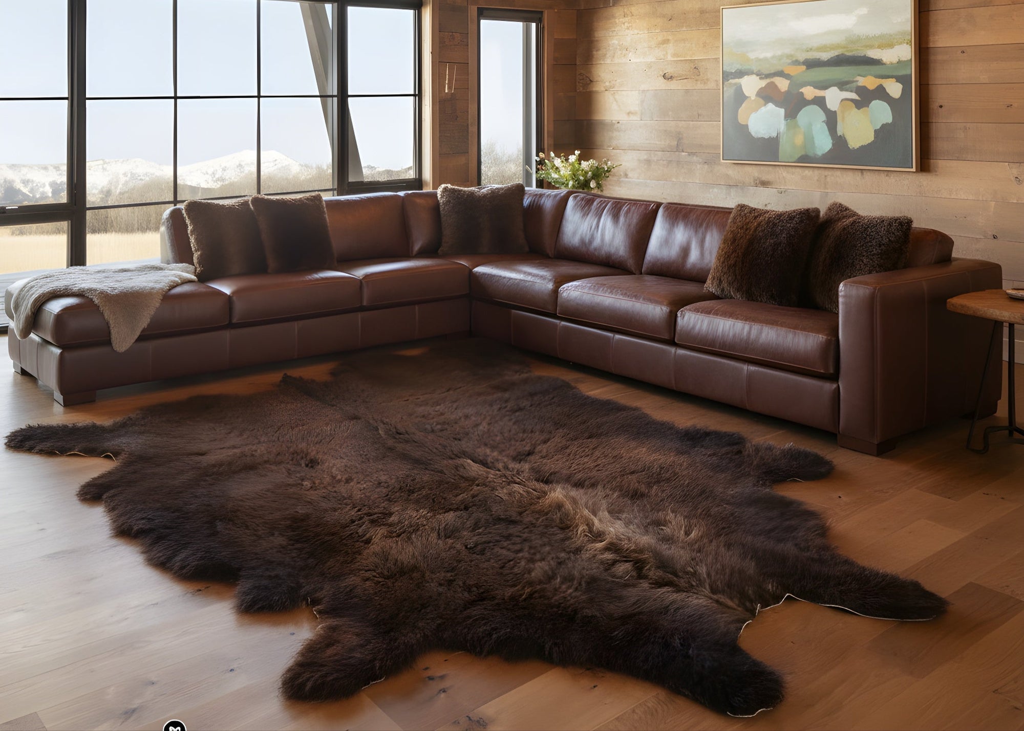 Brown leather sectional sofa in a room with wooden walls, large windows, and a bison rug.