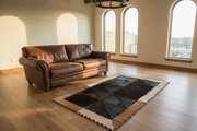 Brown leather sofa in a room with large windows and a patterned rug.
